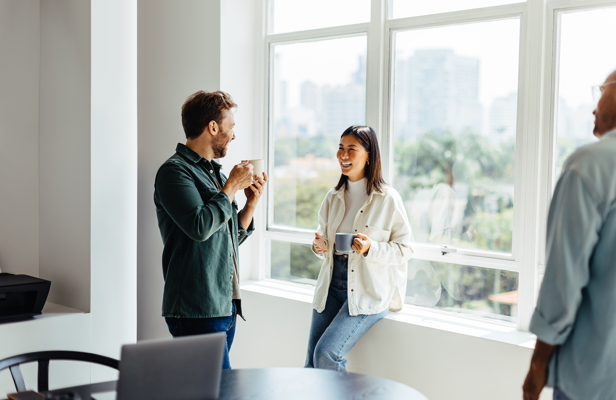 Two colleagues laughing over a cup of coffee in a bright office