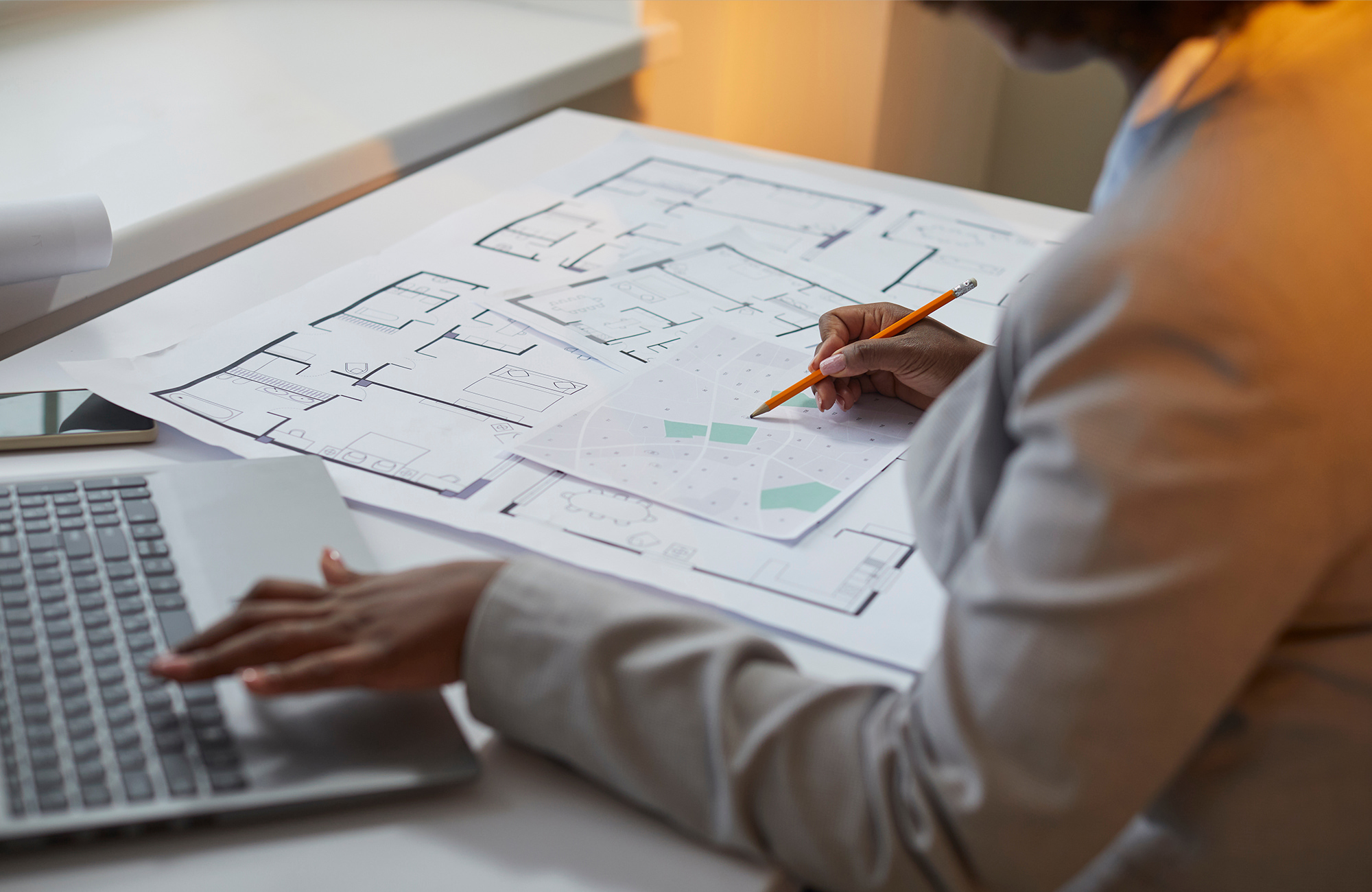 Female architect looking at housing development plans on a table with a laptop